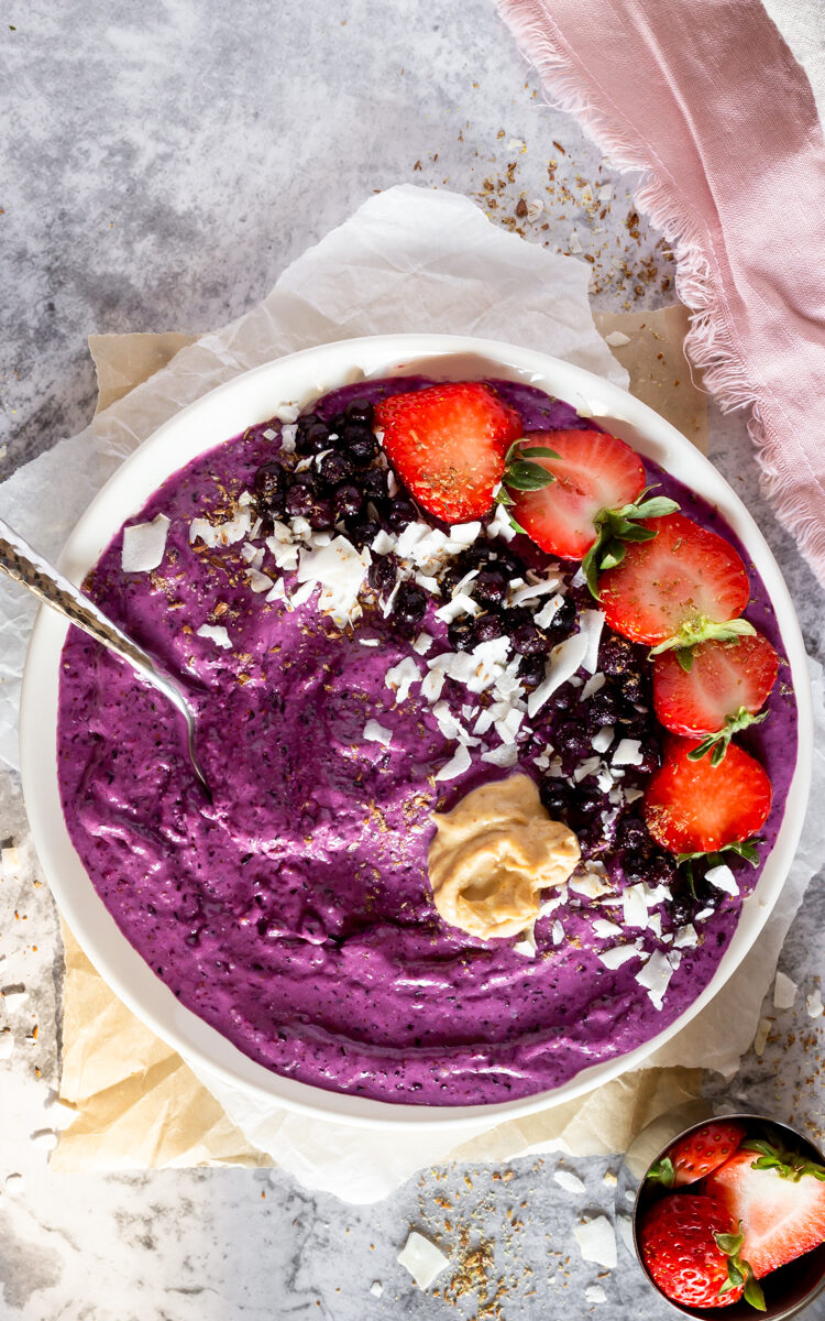 Vegan Blueberry Smoothie Bowl beautifully arranged with fresh strawberries, blueberries, coconut shreds, and peanut butter in a bowl.