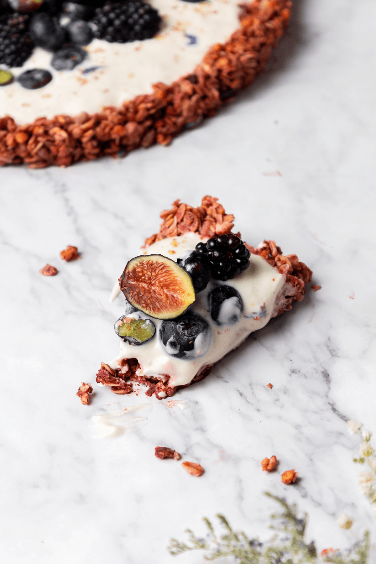 a slice of granola pizza on marble topped with figs and blueberries