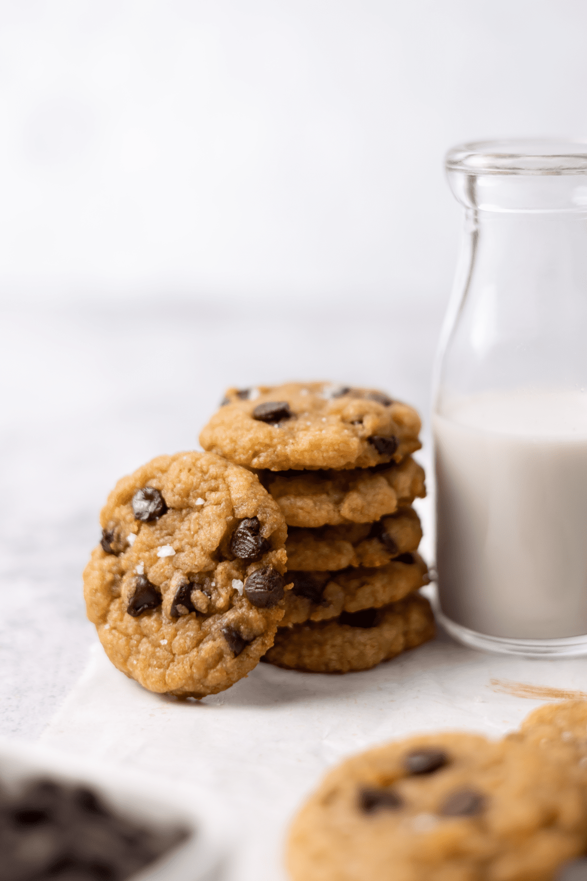 miso chocolate chip cookie leaning against a stack of cookies next to a jar of oat milk