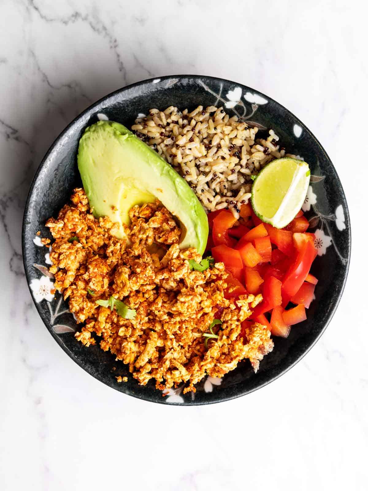 Chipotle Sofritas served in a bowl with avocado fresh bell pepper, brown rice and quinoa and a lime slice.