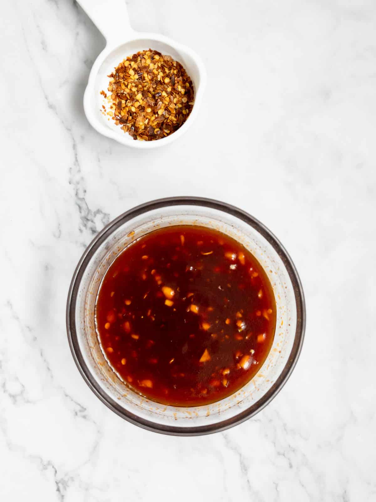 A homemade spicy sauce for rice cakes in a bowl. Next to it is a small bowl of chili flakes.
