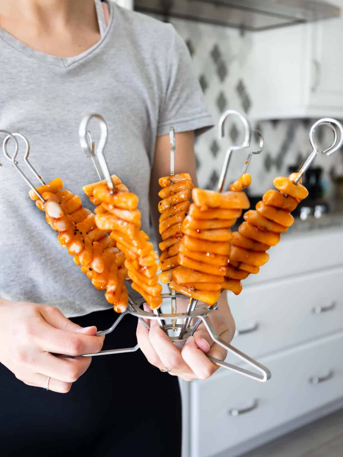 A person holding the glazed vegan Tteokbokki on skewers assembled in the O-yaki skewer system before grilling.