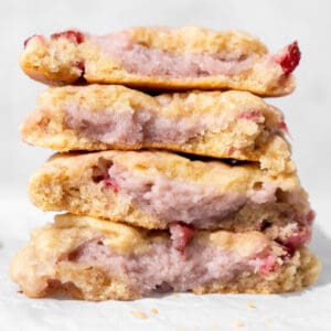 A stack of vegan strawberry cheesecake cookies broken in half. You can see the texture and strawberry cream cheese filling inside the cookies.