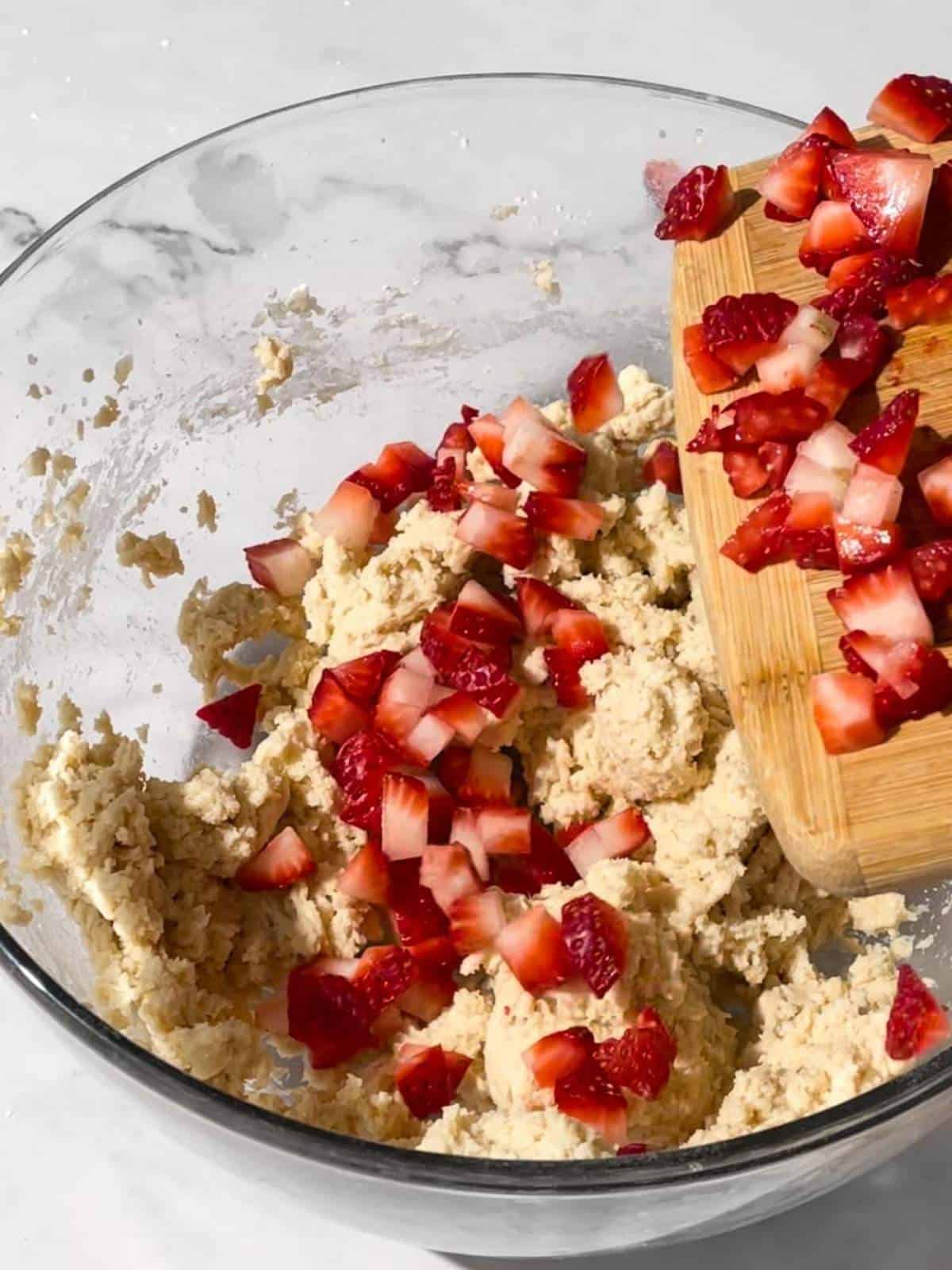 Freshly chopped strawberries are added to a bowl of raw cookie dough.