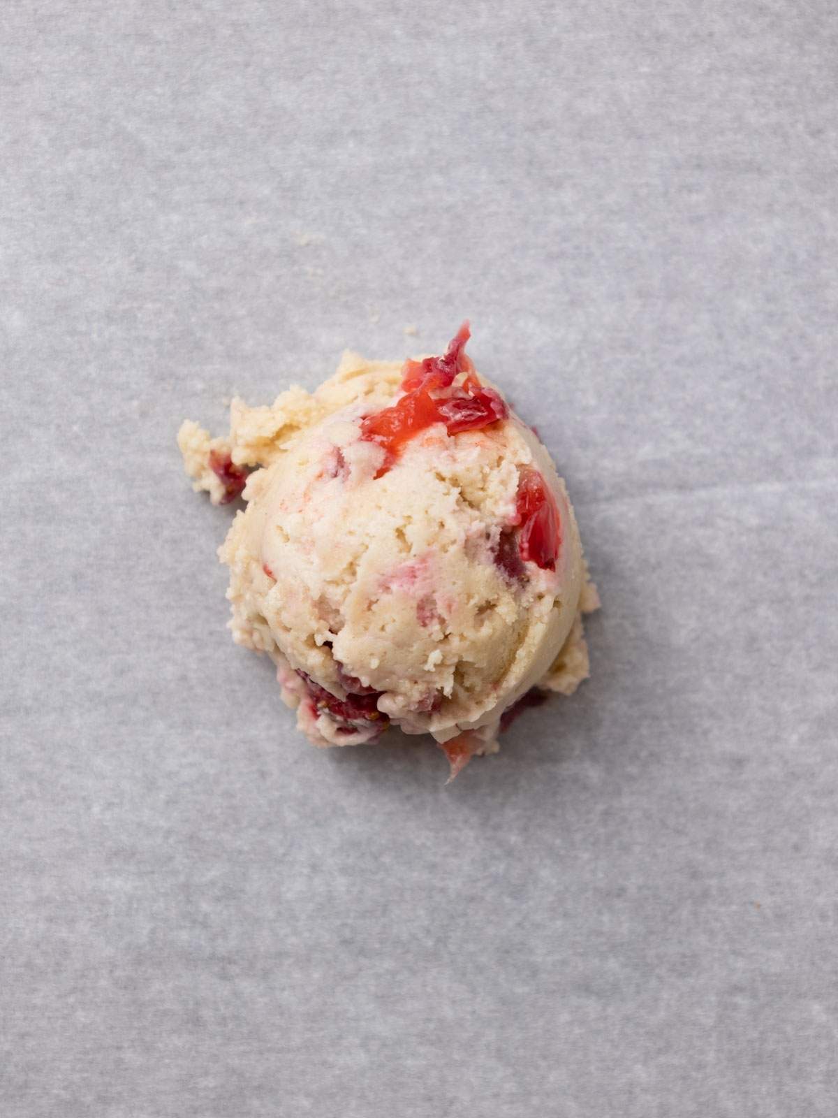 A ball of raw vegan strawberry cheesecake cookie dough ball.