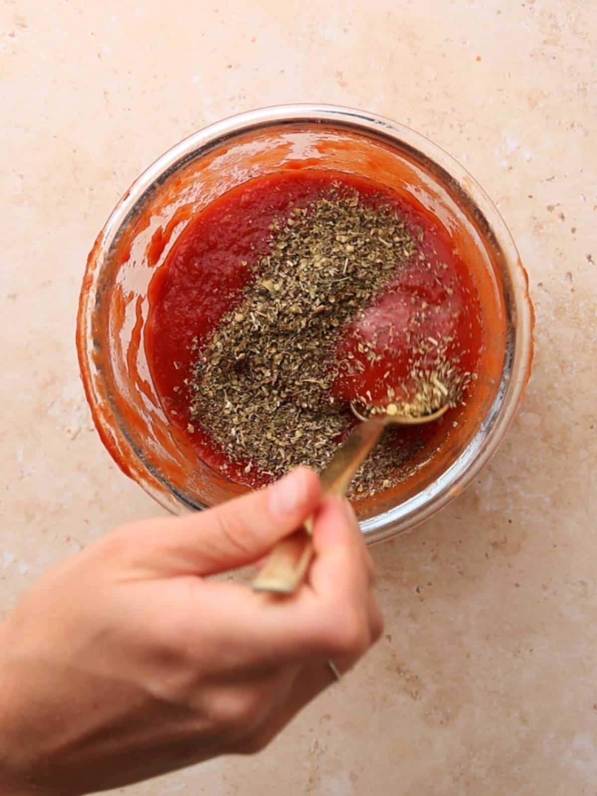 Mixing Italian herbs with tomato sauce.
