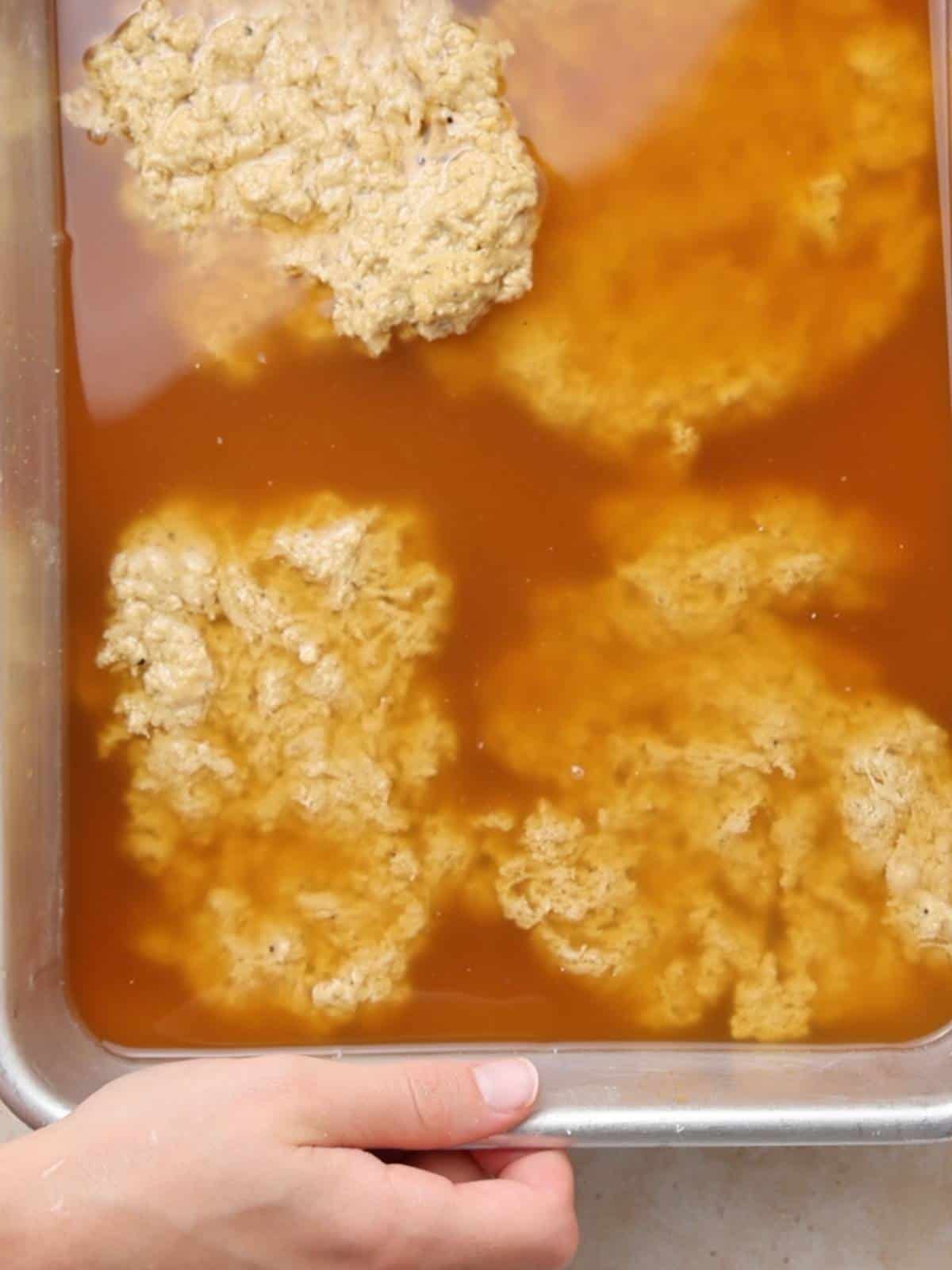 Adding seitan cutlets to broth in a baking dish to cook.