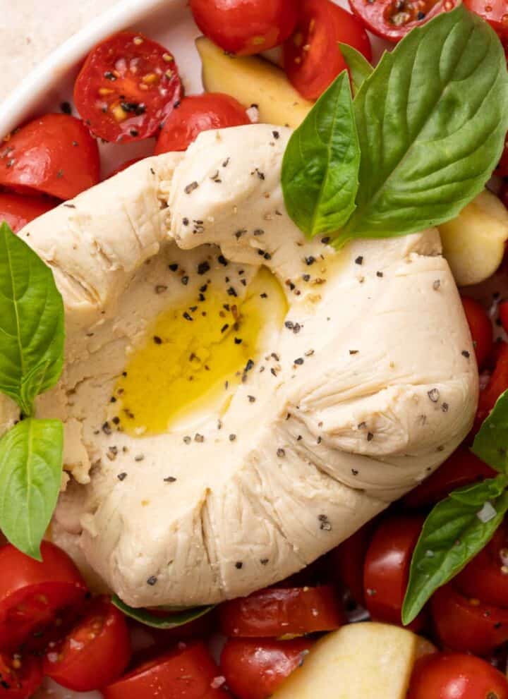 Vegan Burrata served with cherry tomatoes, fresh basil, salt, pepper, and olive oil drizzles.