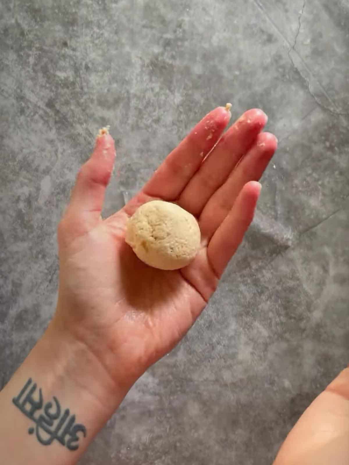 Oiled hand holding vegan cocktail sausage dough formed into a ball.