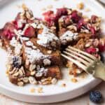 A fork cutting into Cinnamon Crunch French Toasts served on a plate with fresh berries.