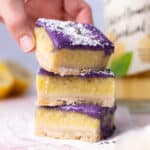 Three slices of lemon lavender bars stacked upon each other. A hand is grabbing the bar slice on top.